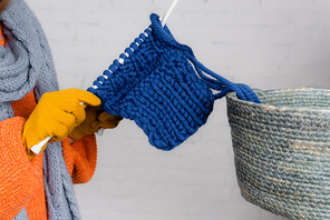 Cropped view of woman in gloves knitting near basket on white background