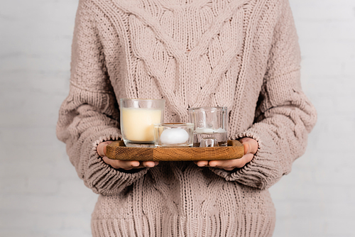 Cropped view of woman in warm sweater holding candles on wooden board on white background