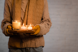 Cropped view of burning candles in hands of woman in warm clothes and gloves on grey background