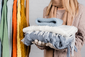 Cropped view of woman holding knitwear near hanger rack with sweaters on white background
