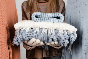 Cropped view of knitwear in hands of woman on blurred background near sweaters on white background