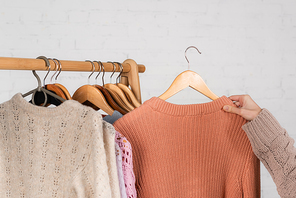 Cropped view of woman holding warm sweater near hanger rack on white background