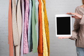 Cropped view of woman holding digital tablet with blank screen near warm sweaters on white background