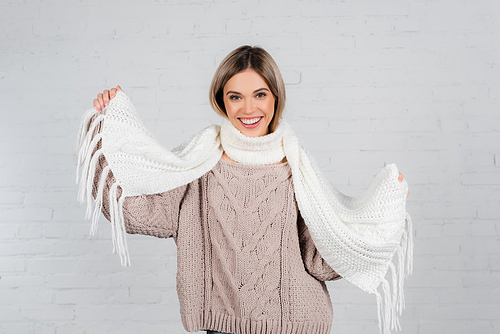 Smiling woman in knitted sweater holding scarf on white background