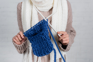 Cropped view of woman knitting with woolen yarn on white background