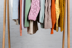 Knitted sweaters on wooden hanger rack on white background
