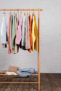 Wooden hanger rack with colorful knitted sweaters near white brick wall
