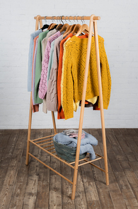 Warm knitted sweaters and gloves on hanger rack near white brick wall