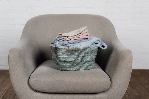 Basket with knitted sweater and gloves on armchair at home