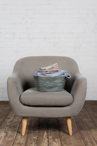Basket with warm sweater and soft gloves on armchair