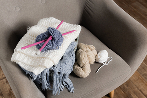 High angle view of knitting needless, yarn and sweater on armchair at home