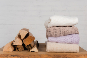 Wooden logs near warm knitted sweaters on table on white background