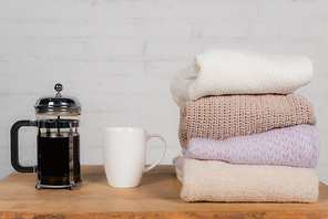 Cup and teapot near knitted sweaters on table on brick wall background