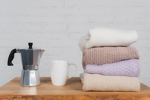 Coffee maker, cup and woolen sweaters on wooden table