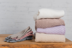 Gloves and cozy sweaters on wooden table with brick wall at background