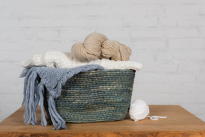 Woolen yarn in basket on wooden table on white background