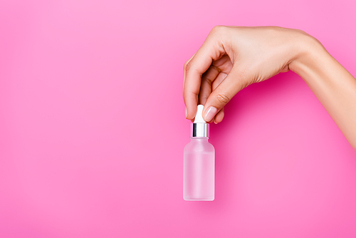 partial view of woman with bottle of cuticle remover on pink background