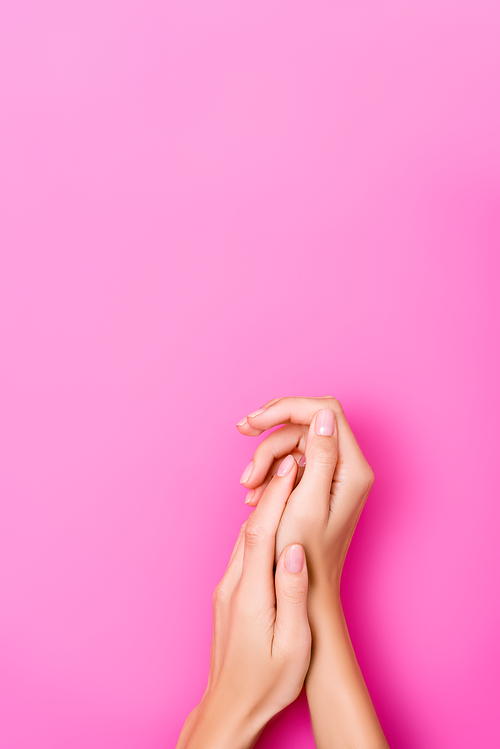 top view of female hands with fingernails covered with pastel enamel on pink background