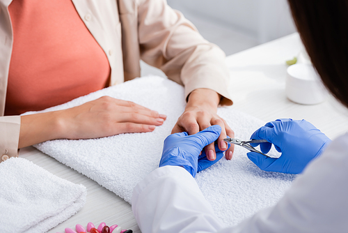 partial view of manicurist cutting cuticle with nipper while making manicure to client, blurred foreground