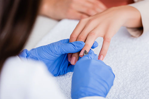 partial view of manicurist cutting cuticle with nipper while making manicure to woman, blurred foreground
