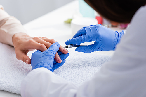 partial view of manicurist holding cuticle nipper near hand of woman, blurred foreground