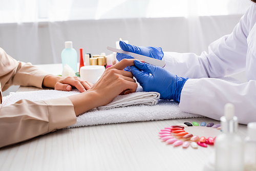 cropped view of manicurist holding nail file while making manicure to client on blurred foreground