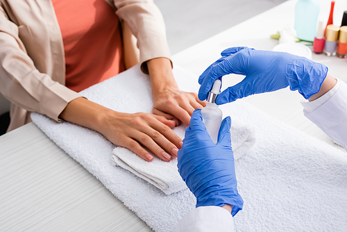 partial view of manicurist holding cuticle remover near client in nail salon