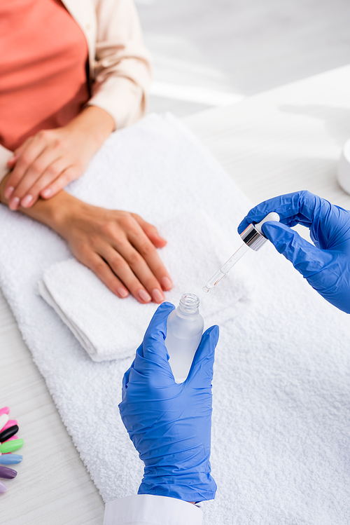 cropped view of manicurist holding cuticle remover near client on blurred background