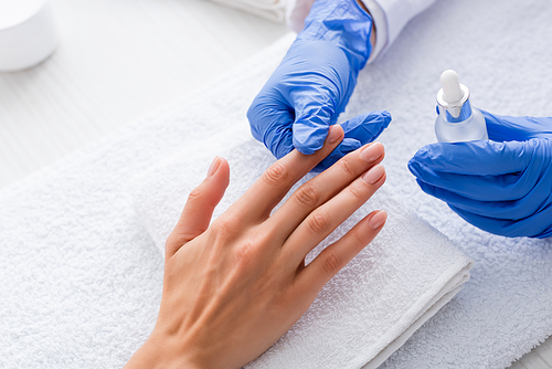 partial view of manicurist holding cuticle remover while touching finger of client
