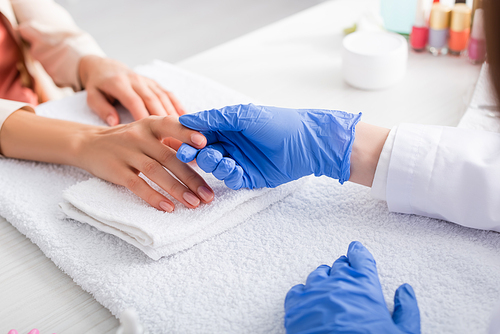 cropped view of manicurist in latex gloves touching finger of client