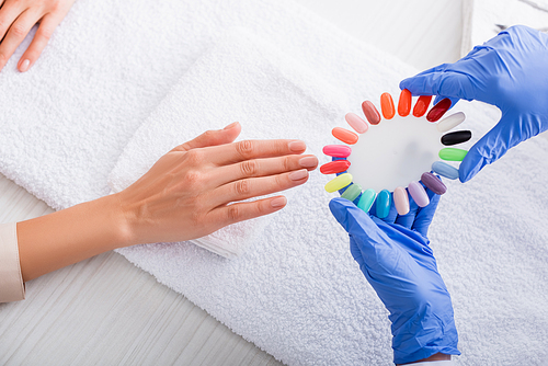 partial view of manicurist holding samples of colorful artificial nails near hand of client