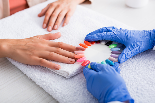 cropped view of manicurist holding set of multicolored artificial nails near hand of client, blurred background