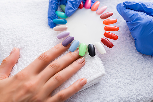 partial view of manicurist holding set of multicolored false nails near hand of client