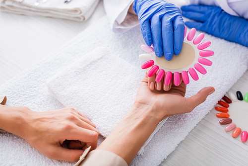 cropped view of manicurist holding palette of artificial nails near hand of client