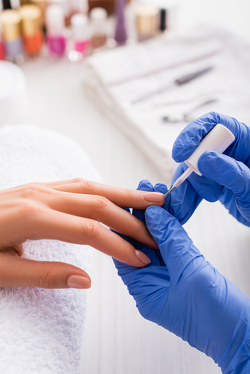 cropped view of manicurist in latex gloves applying nail polish while making manicure to woman