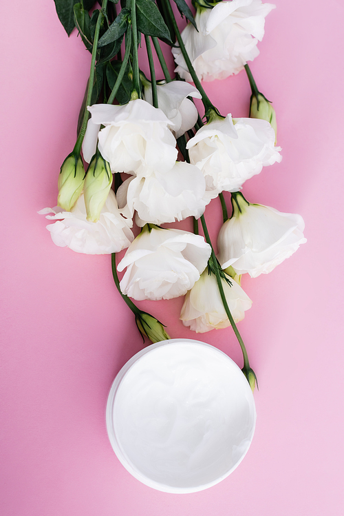 top view of cosmetic cream and white eustoma flowers on pink background