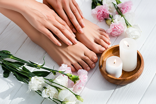 female feet and hands with glossy pink nails near  and eustoma flowers and candles on white wooden surface