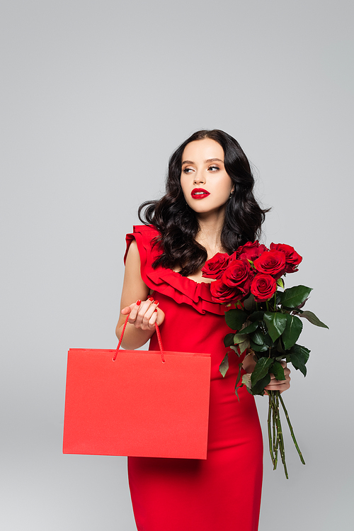 brunette woman holding shopping bag and roses isolated on grey