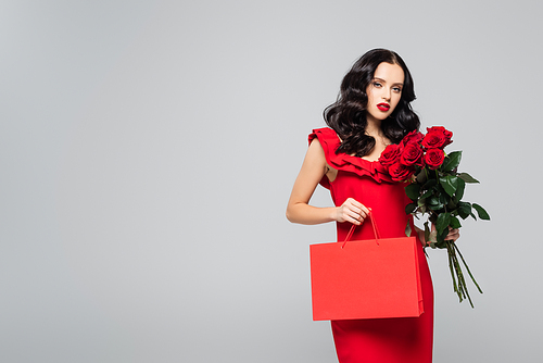 young woman holding shopping bag and red roses isolated on grey