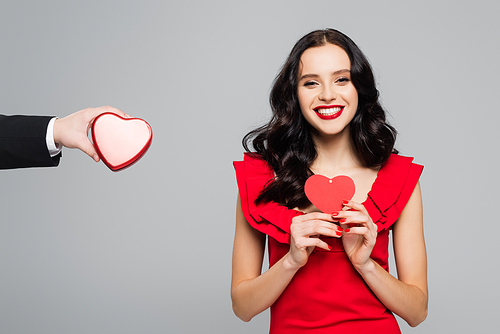 man holding heart-shaped box near happy woman with paper heart isolated on grey