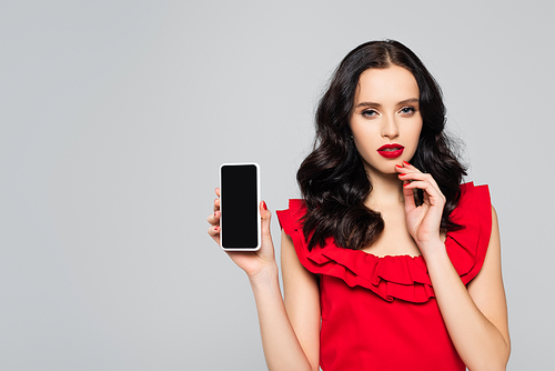 woman with red lips holding smartphone with blank screen isolated on grey