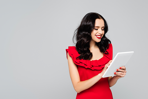 cheerful woman with red lips using digital tablet isolated on grey