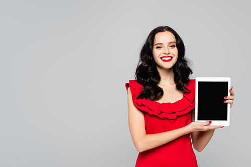 cheerful woman with red lips holding digital tablet with blank screen isolated on grey
