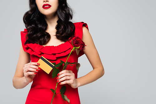 cropped view of brunette woman holding red rose and credit card isolated on grey