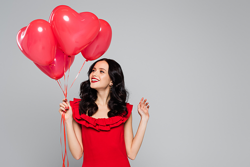 happy woman holding red heart-shaped balloons isolated on grey