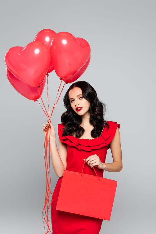 young woman holding red heart-shaped balloons and shopping bag isolated on grey