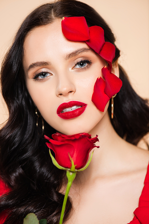 brunette young woman with red lips and petals of rose on face isolated on pink