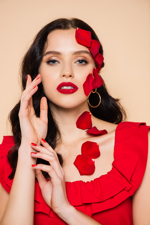 brunette young woman with petals of red rose on face isolated on pink