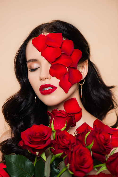 young woman with closed eyes and petals on face near roses isolated on pink