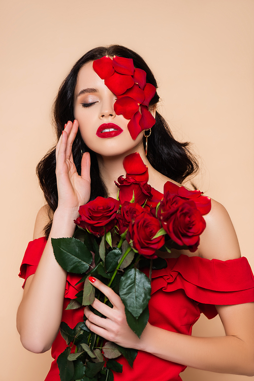 brunette woman with closed eyes and petals on face near roses isolated on pink